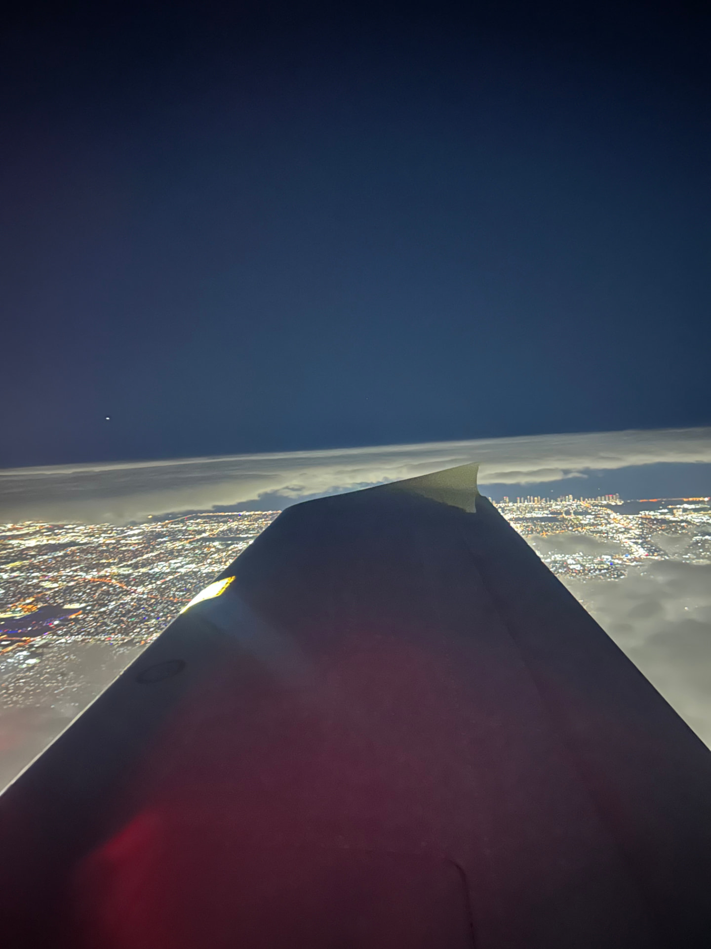 Aircraft wing over a city glowing at night above the clouds